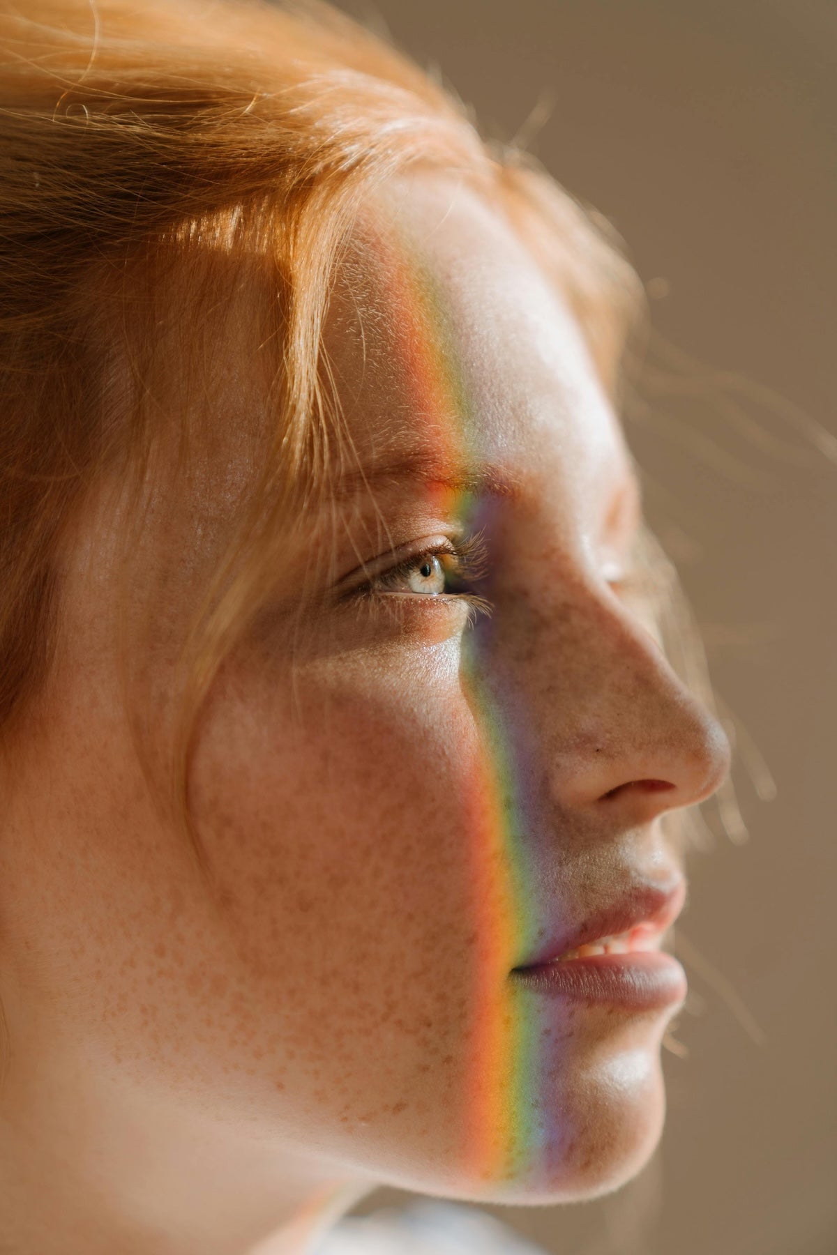 Close-up of a person with a rainbow reflection on their face against a neutral background